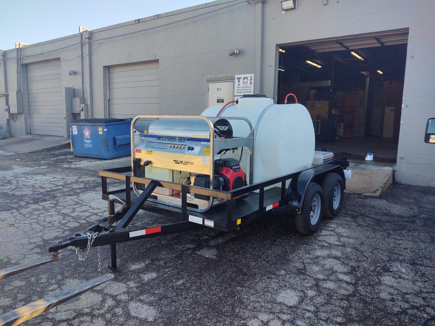 A trailer with industrial cleaning equipment and a power generator parked outside an industrial garage.
